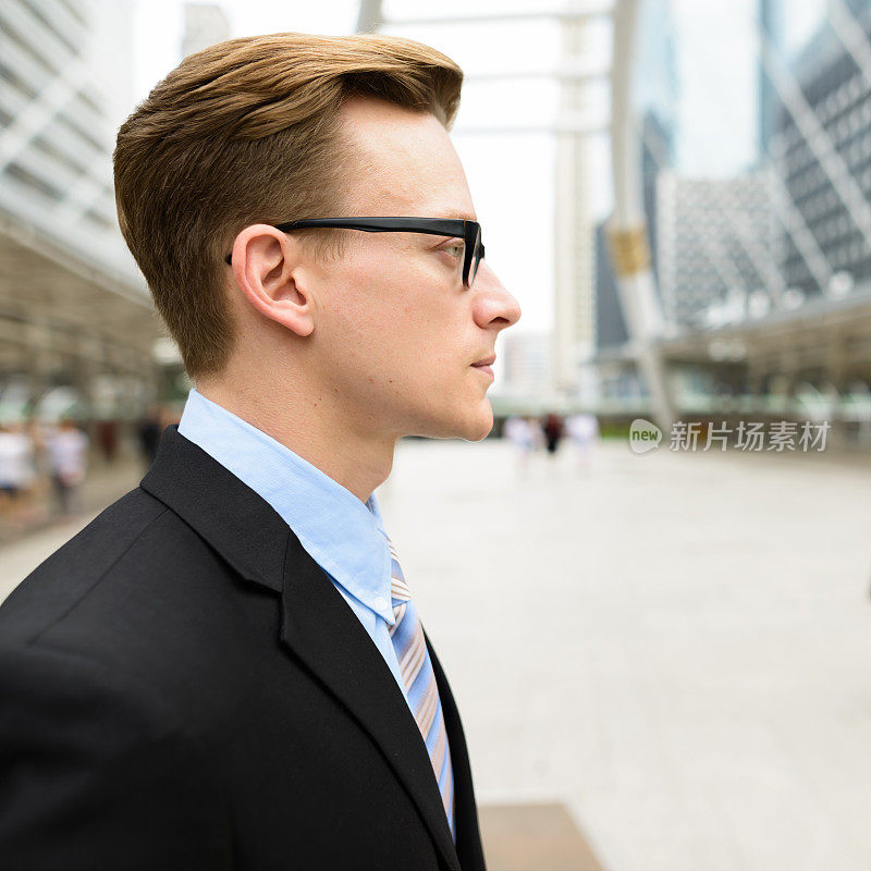侧面视图年轻英俊的商人戴眼镜反对在曼谷城市的现代建筑的观点