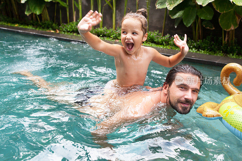 幸福的家庭，活泼的父亲和年幼的孩子，可爱的蹒跚学步的女儿，在游泳池里玩得很开心。