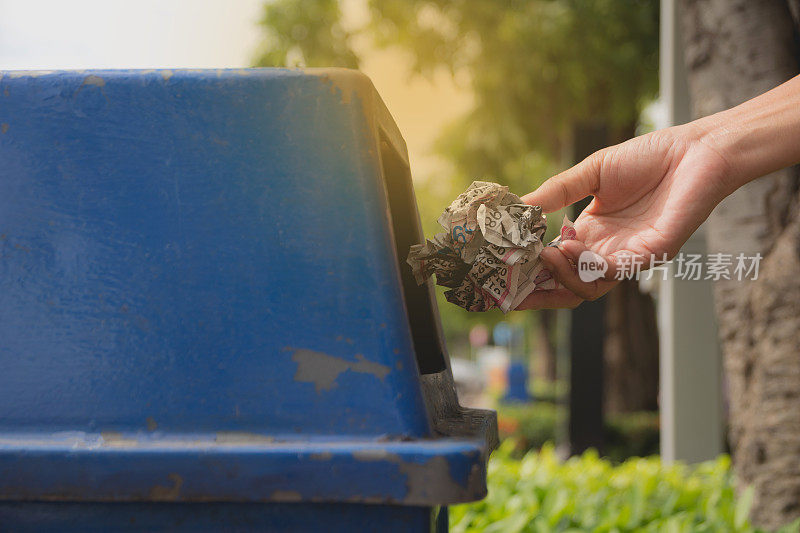 女性的手把皱巴巴的纸扔进蓝色的塑料垃圾桶。