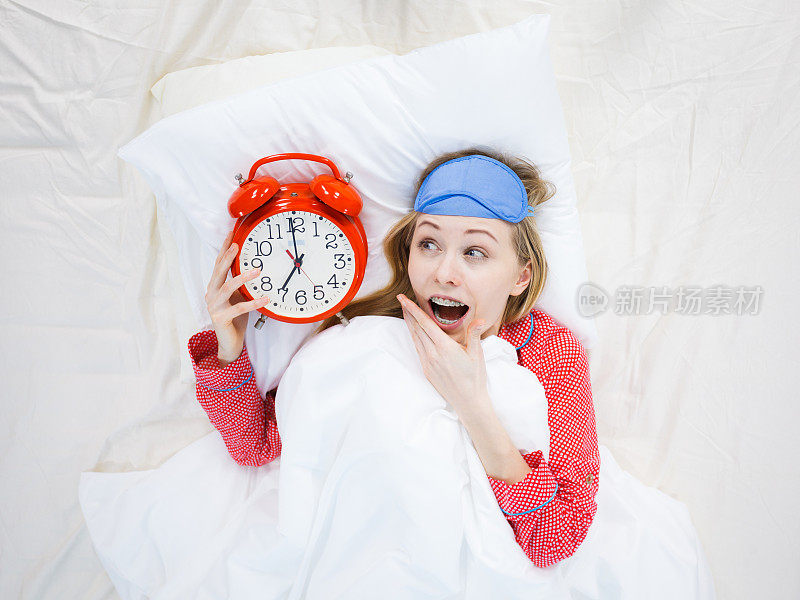 震惊的女人穿着睡衣拿着闹钟睡过头了