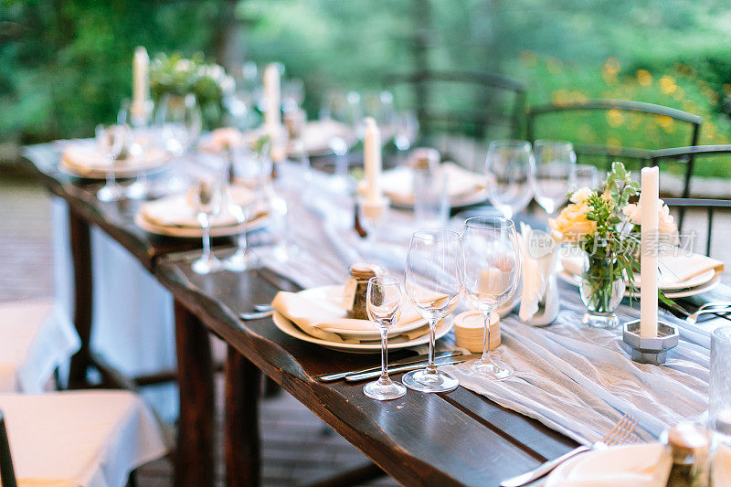 盛宴，晚餐，传统观念。长长的橡木桌子用于庆祝银器，盘子和透明的耀眼的眼镜，鲜花和蜡烛在有趣的八角形的持有者