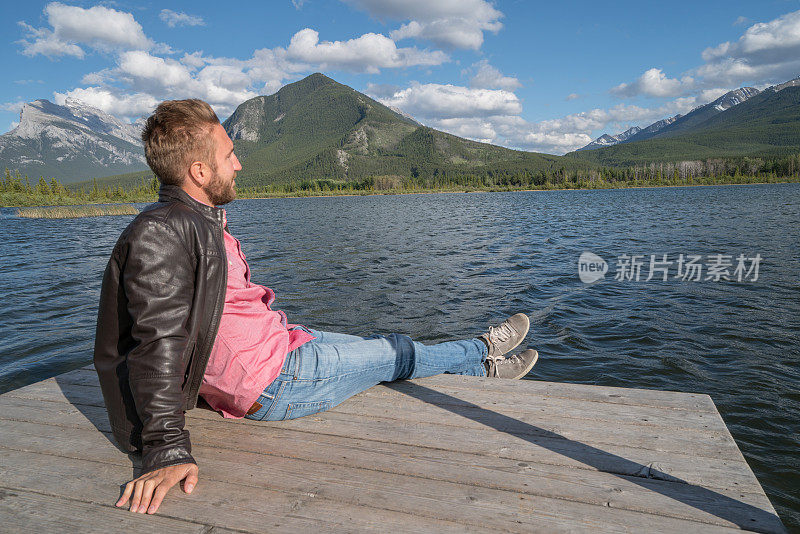 年轻男子坐在湖墩上凝视山景