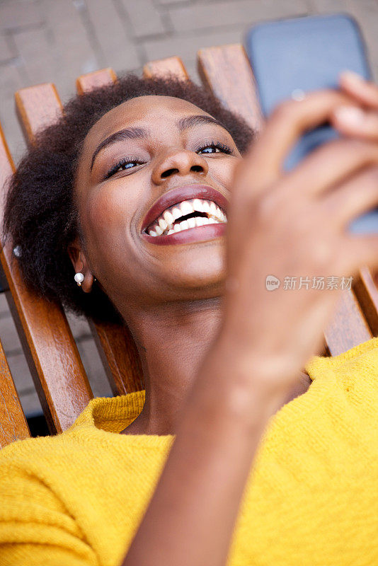快乐的非裔美国女人坐在外面看手机