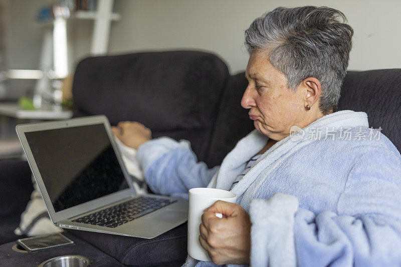 高级女性在家生病时使用笔记本电脑