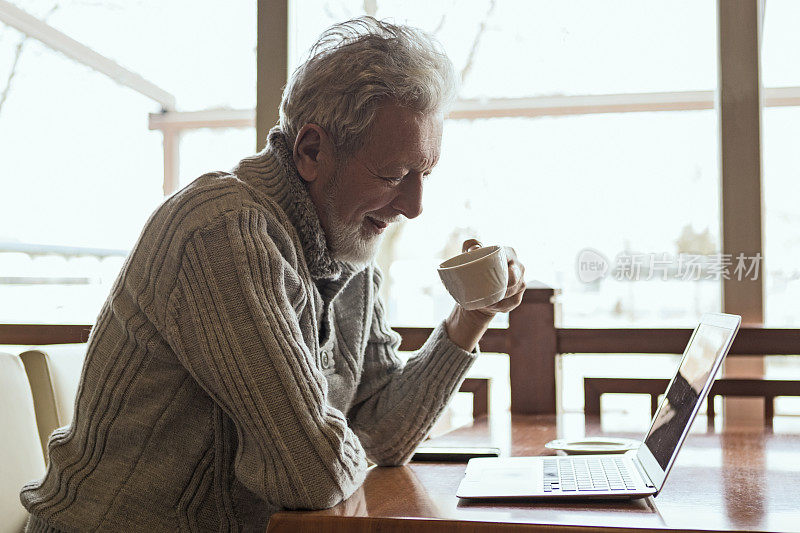现代高级男子使用笔记本电脑和喝咖啡在咖啡馆