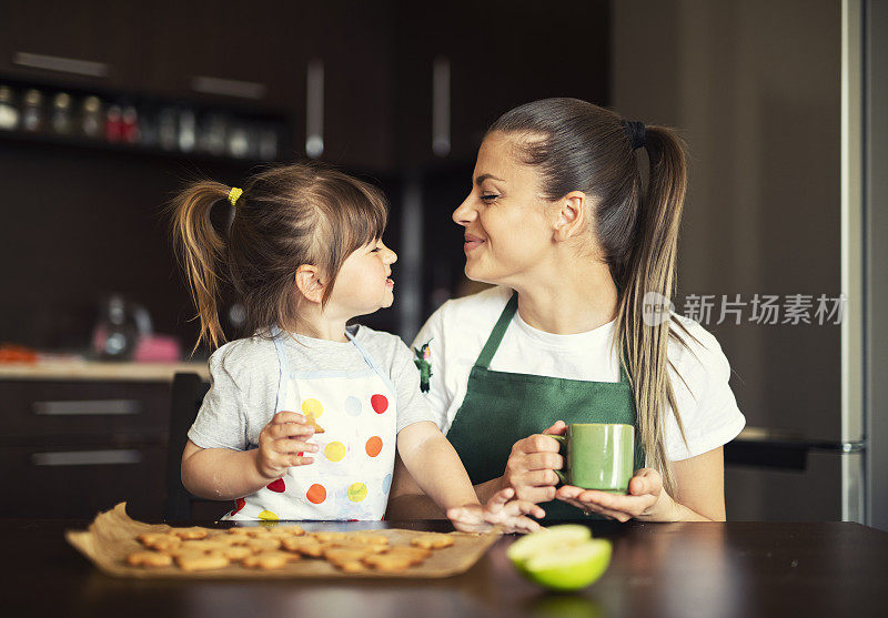 快乐的家庭与烤饼干，母亲和女儿有乐趣和吃新鲜热饼干