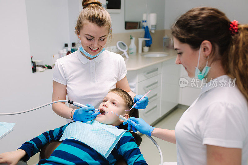 儿童牙医兼助理检查男孩的牙齿，他坐在牙科诊所的椅子上。女牙医