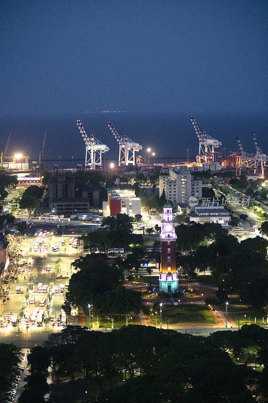 Torre纪念性钟楼在夜晚与布宜诺斯艾利斯港口远处灯火通明