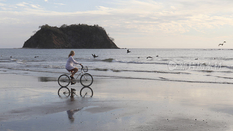 日出时分，一名女子骑着自行车沿着热带海滩骑行