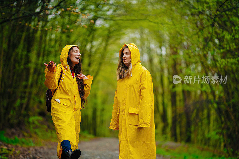 两个穿着雨衣的女性朋友在雾霾的森林里在雨中奔跑