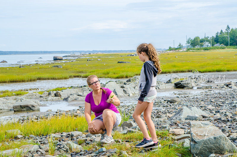 一个女人和一个女孩在岸上收集可食用的植物