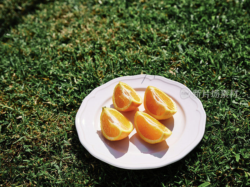 在一个阳光明媚的夏日，外面的绿草地上，在一个白色盘子上切成四分之一的橙子。