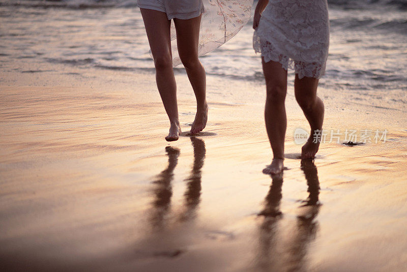 两个女人在沙滩上的细节和她们在湿沙上的倒影