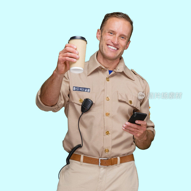 身穿警徽、手持咖啡杯、使用短信的男性警察站在蓝色背景前