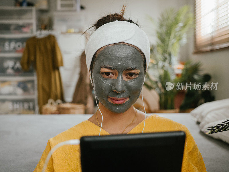 年轻女子敷面膜，在家使用平板电脑。