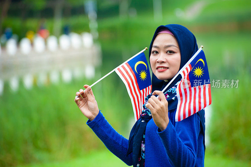 年轻的马来西亚妇女挥舞着马来西亚国旗，带着崇高的爱国主义精神庆祝独立日