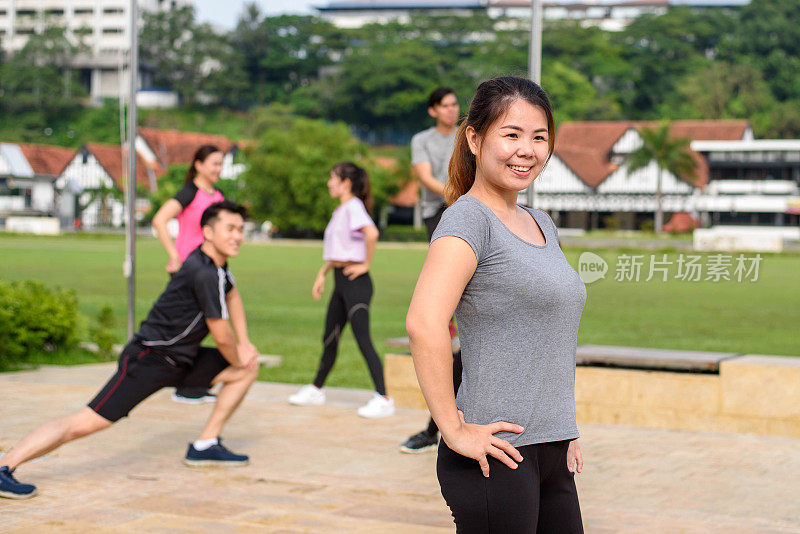 一个亚洲女人和她的朋友在运动服装热身和伸展在户外人行道上锻炼