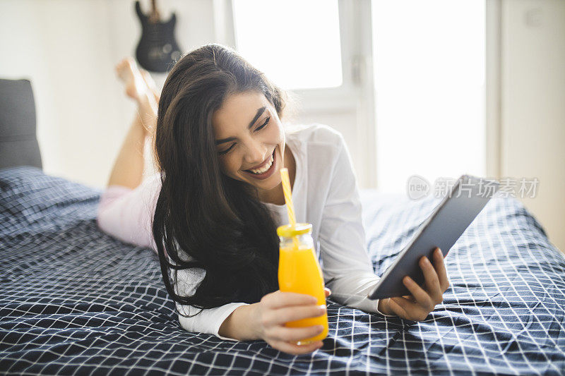 快乐的女人看报纸，喝果汁，早上躺在床上