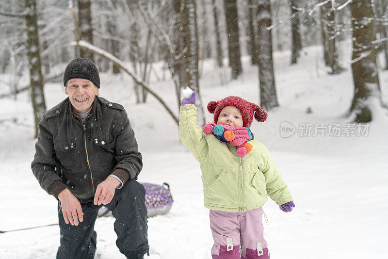 孙辈是老年人快乐和活跃的关键。70岁的老爷爷和2岁的孙女在冬天的森林里玩雪球