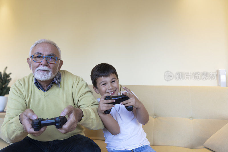 英俊的爷爷和孙子一起在家玩游戏机。