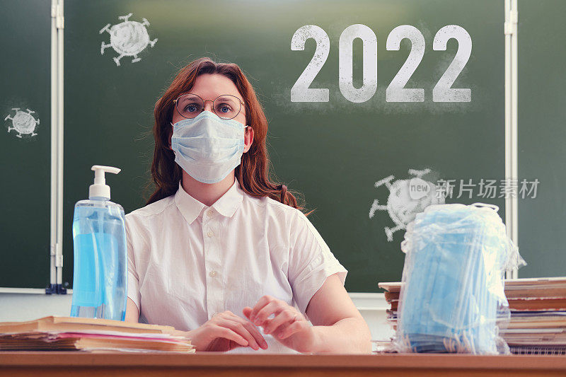 女老师在课堂上用粉笔在黑板上题字2022。新学年的冠状病毒问题，复制空间