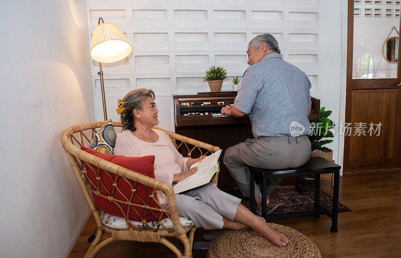 一对亚洲老夫妇在家里的客厅里一起弹钢琴、唱歌。