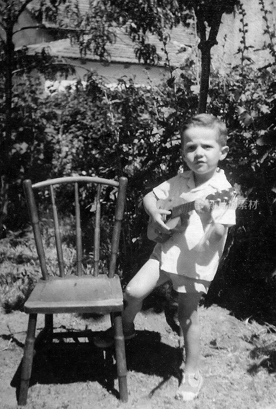 照片拍摄于60年代早期，小男孩在自家后院弹吉他