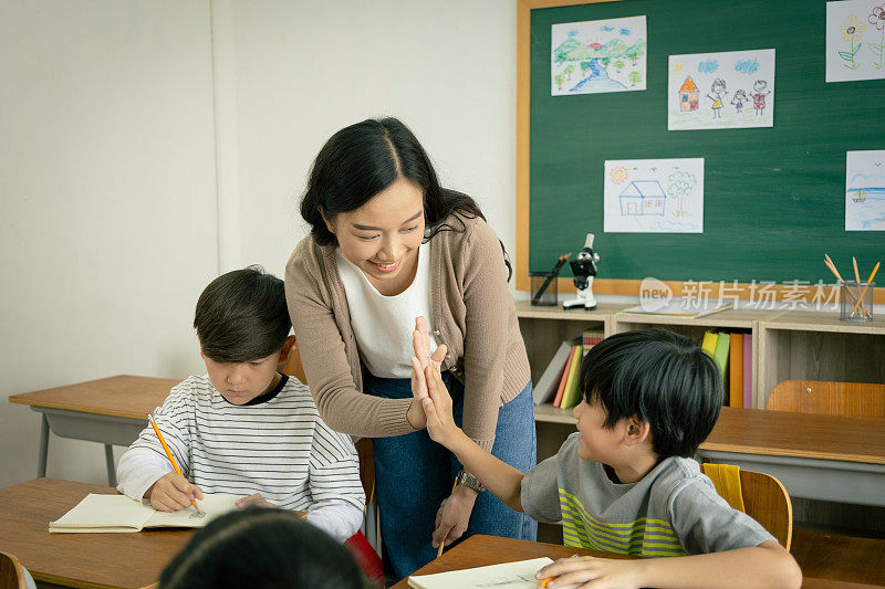一位年轻的亚洲女教师和一个小学男孩在教室里拍手。老师祝贺学生们的成功