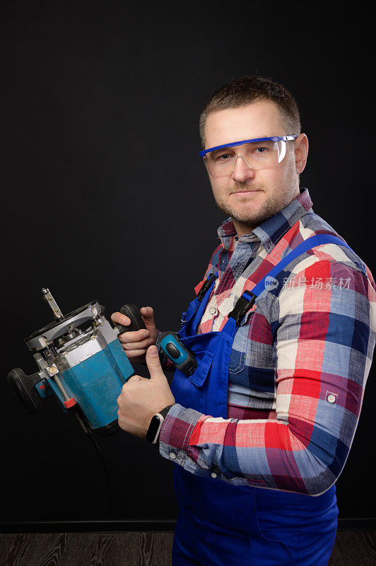 白人男性修理工戴着眼镜，手里拿着木工工具，翘起大拇指。一个木匠的肖像在一个黑色的工作室背景。批准的概念