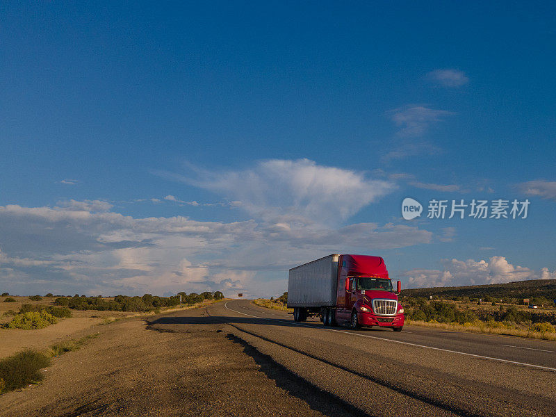 黄昏时分，在戏剧化的天空下，半卡车在犹他州沙漠的高速公路上超速行驶