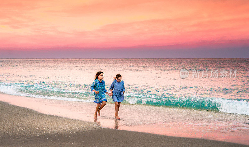两个孩子，姐妹，在史诗般充满活力的夕阳下，一起在田园诗般的海滩上