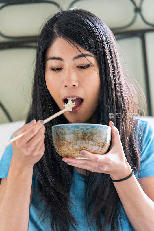 亚洲女人坐在床上吃米饭