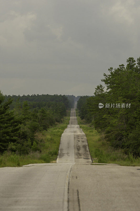 低角度视角，穿过云雾缭绕的山丘，在沙松林中，一条笔直的柏油路