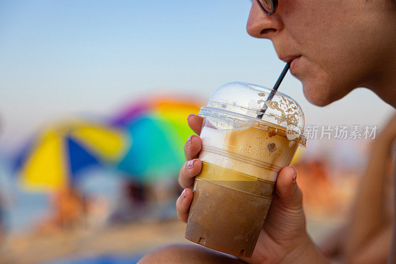 在海滩上，一个不认识的女人用塑料杯喝冰咖啡