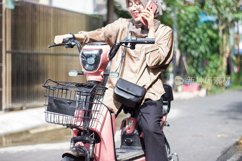 年轻的伊斯兰妇女在居民区骑电动自行车