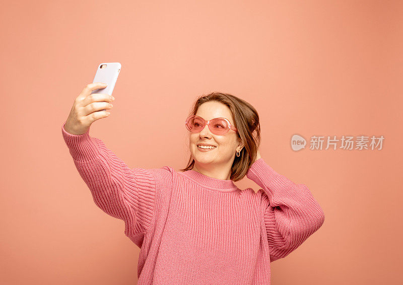 愉快的女子站在粉红色的背景墙孤立地打电话的图像。