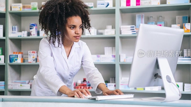 非洲女药剂师在药店的电脑上检查药品。在药店药店工作的非裔美国药剂师。