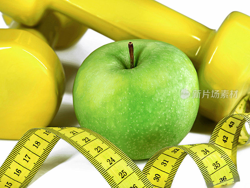 白色背景上的卷尺、绿色苹果和黄色哑铃的特写，健康的生活方式和健身理念