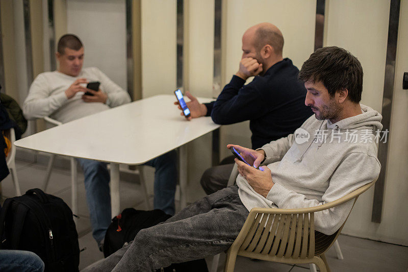 三个年轻人坐在一起，每个人都在玩手机
