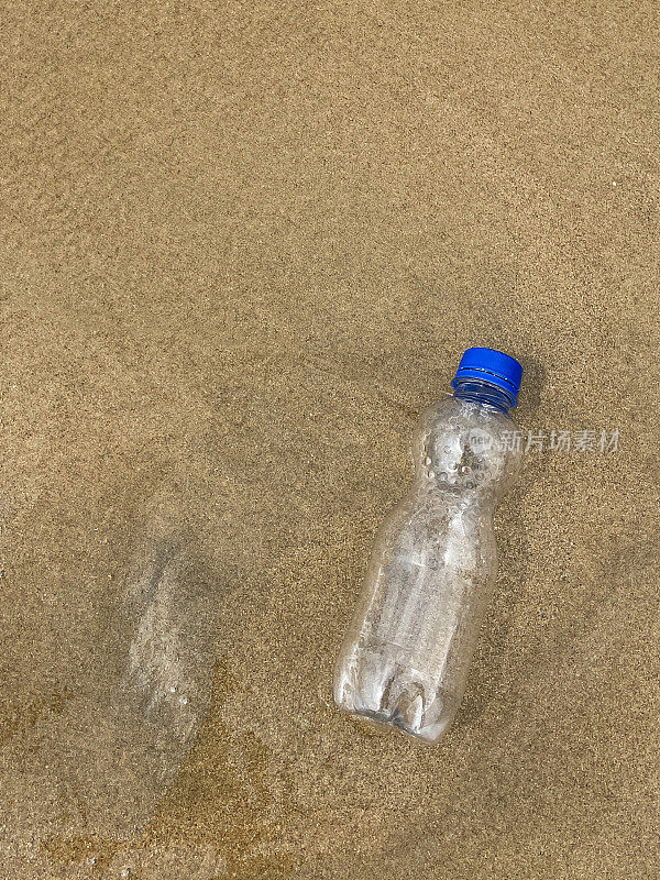 图片:退潮时被冲到沙滩上的蓝色盖子的空透明塑料水瓶，海岸上的海洋垃圾和污染，乱扔的沙子，肮脏的海滩，高架视图，复制空间