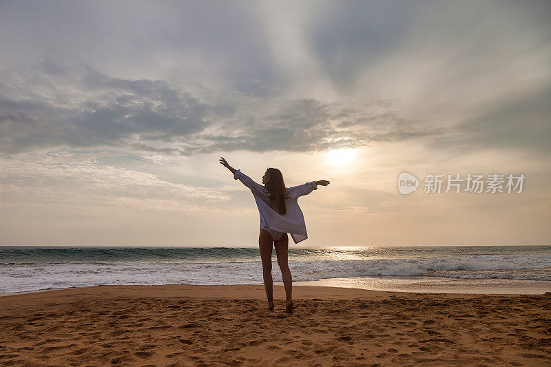 后视图年轻女子在白色衬衫摆姿势与手侧在海洋背景，夏天。在热带海上享受轻松愉快的假期。旅游度假度假概念。复制广告文字空间