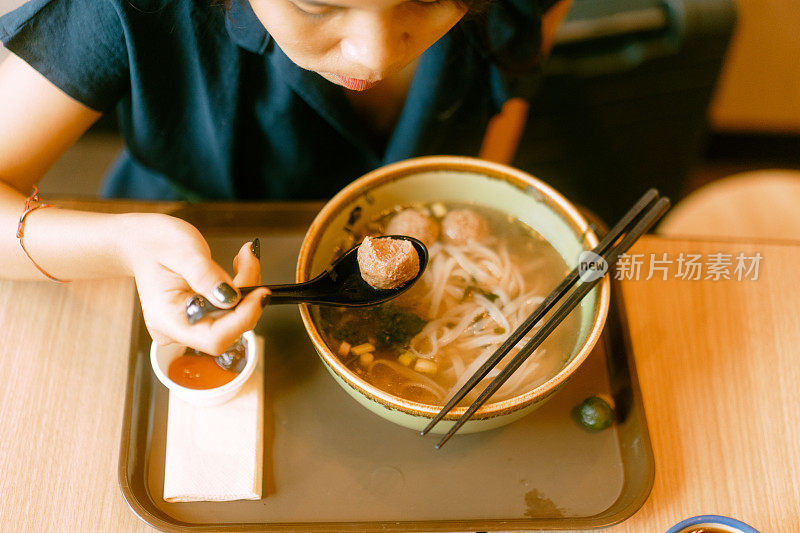 一个亚洲女人独自在餐厅吃着大粉面，喝着越南咖啡