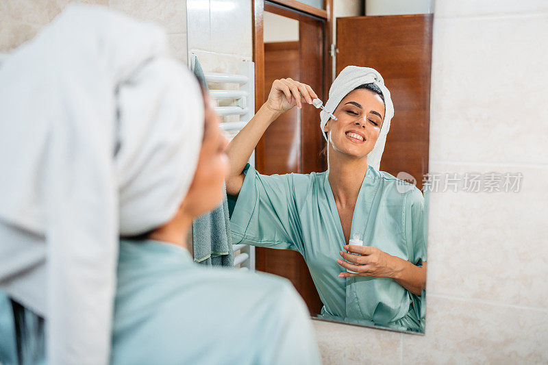 年轻女子在浴室的镜子前擦脸油