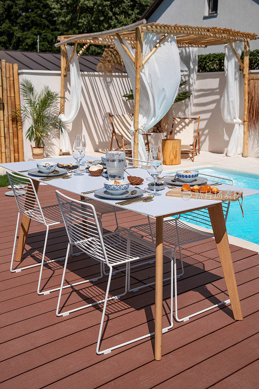 室外花园生活空间，餐桌设置在游泳池旁边的木露台露台上
