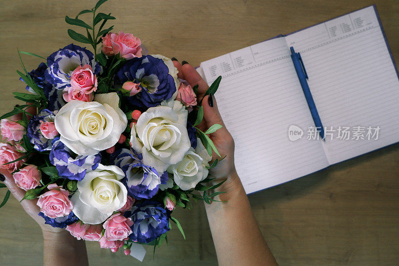 Flatlay。女性手中捧着一束五颜六色的玫瑰花。笔记本，在木桌上用笔写日记