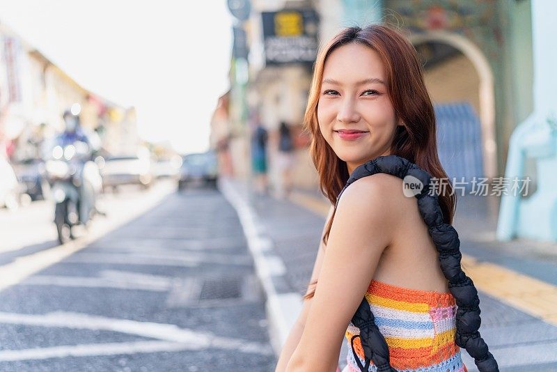 这位Z世代亚洲女性在普吉岛老城的路边摆出可爱的姿势，在她的旅行冒险中享受着放松的时刻