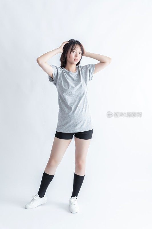 身穿灰色t恤和黑色短裤的年轻亚洲女子双手抱头摆姿势