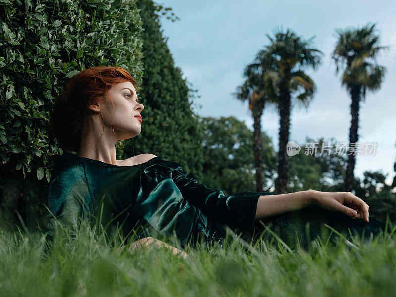 穿着绿色衣服的迷人女子躺在草地上
