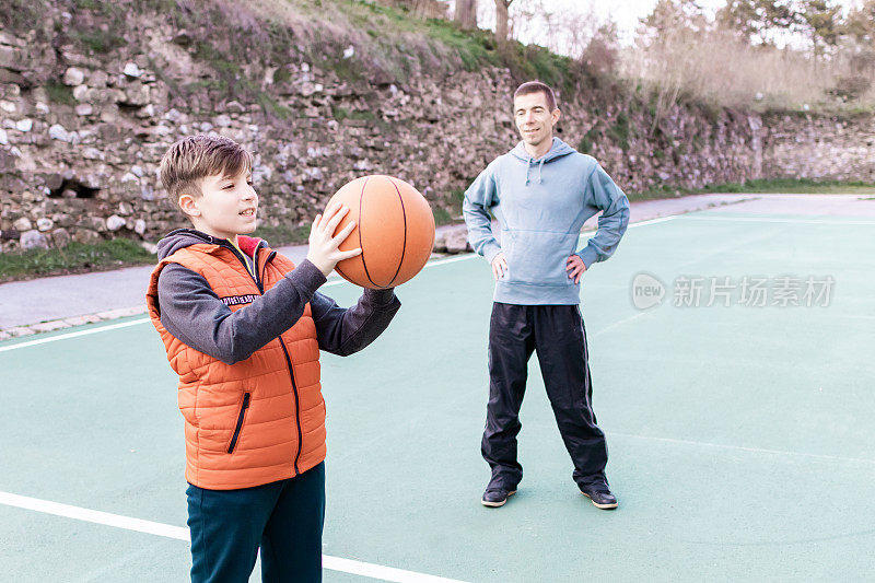 父亲和儿子在球场上打篮球，教小球员。幸福和健康的家庭快乐。户外运动。