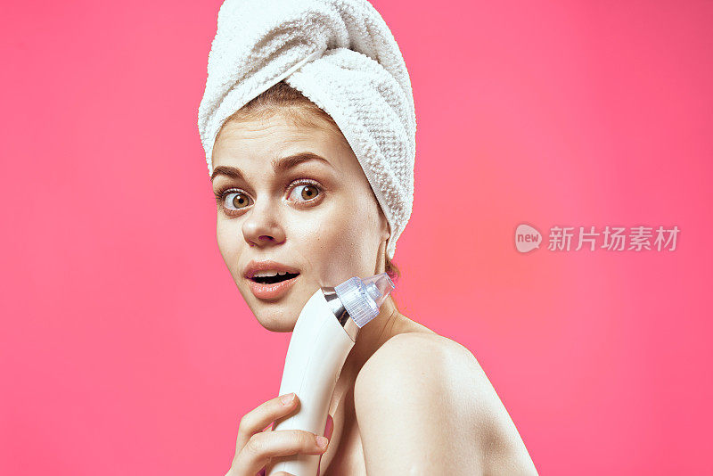 欢快的国民妇女用毛巾在她的头上按摩器在手上皮肤护理水疗护理粉红色的背景